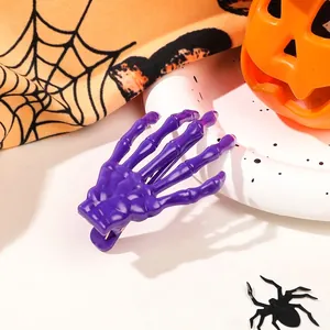 Close-up of a purple skeleton hand hair clip with Halloween pumpkin and spider web backdrop