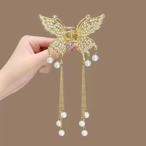 Close-up of golden butterfly hair claw clip with rhinestones and long pearl tassels