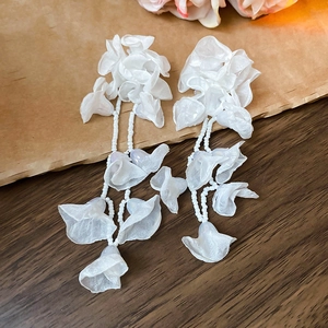 Close-up of white chiffon flower earrings with delicate bead tassels on a wooden surface