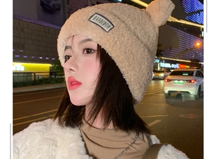 Close-up of beige plush teddy bear winter hat with cute ears and purple label detail