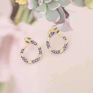 Detail of golden snake hoop earrings with blue enamel scales and green gemstone eyes