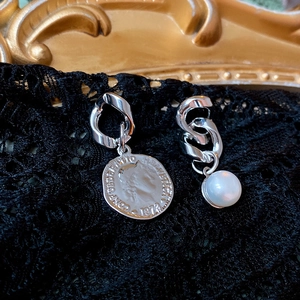 Detailed view of asymmetric silver earrings with a coin pendant and white pearl charm