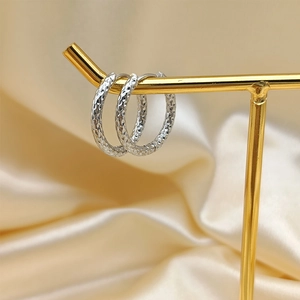 Silver hammered texture hoop earrings on a gold stand with champagne satin background