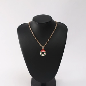 Detail showing a gold necklace with a red bow Christmas wreath pendant on a black bust