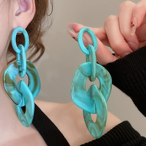 Close-up of geometric chain earrings with green and brown marble acrylic texture on a model