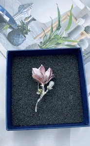 Macro view of magnolia flower brooch with pink gradient petals and green leaf detail