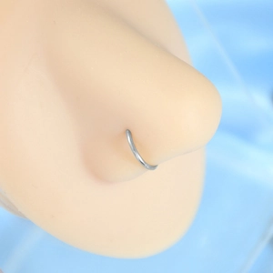 Macro shot of silver D-shaped stainless steel nose ring on a nose model