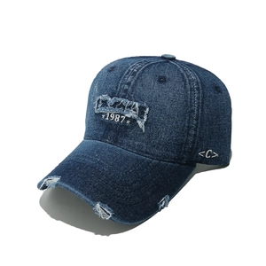 Close-up of distressed denim baseball cap with 1987 embroidery and frayed ripped edges