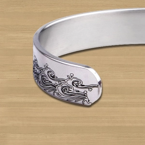 Close-up of engraved wave pattern detail on stainless steel cuff bracelet with brushed finish