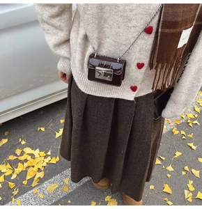 Detail of a mini dark brown glossy leather chain bag styled with a vintage knit sweater