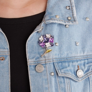 Close-up of a floral enamel brooch with purple petals and rhinestones on a denim jacket