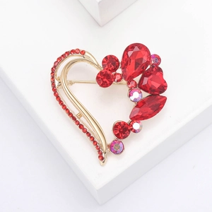 Elegant gold heart brooch with red rhinestones displayed on a white podium