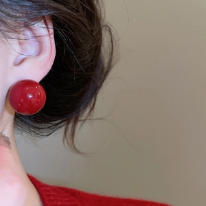 Close-up of elegant red round pearl stud earrings worn by a model in soft lighting