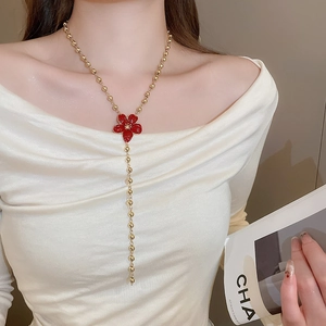 Detail view of long golden bead Y-necklace with vibrant red enamel flower pendant