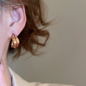 Close-up of golden C-shape earrings with textured metal and burgundy enamel detail