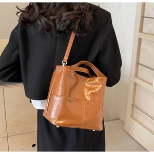 Brown leather tote bag worn as a shoulder bag by a model in a minimal interior setting