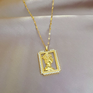 Detailed view of gold square pendant necklace with portrait and cubic zirconia on beige fabric