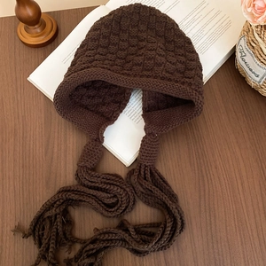 Macro view of dark brown knit earflap hat with long braided tassels and textured checkers