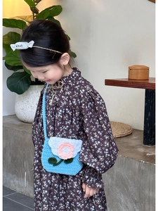 Detail of blue knitted kids crossbody bag featuring a pink 3D flower with green leaves