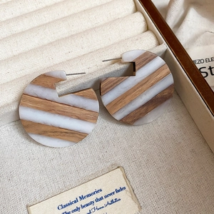 Close-up of retro C-shaped earrings with brown wood and white marble resin stripes