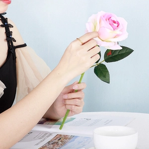 Close-up of a slender gold ring on a finger holding a realistic pink rose for a lifestyle view