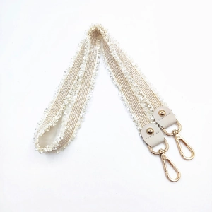 Detail of beige woven shoulder strap with gold metal hooks and bohemian fringe edges