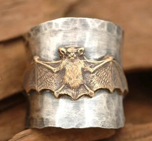 Macro shot of wide textured silver ring with embossed gold bat detail and hammered finish