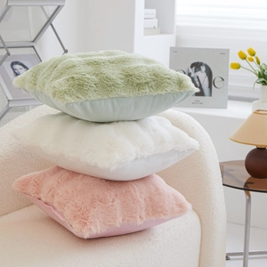 Stack of colorful plush square throw pillows in green, cream, and pink on a soft sofa