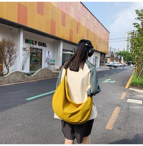 Outdoor street view of a large yellow canvas crescent crossbody bag for daily travel