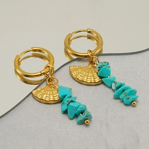 Macro shot of gold fan earrings with natural turquoise beads on a reflective surface
