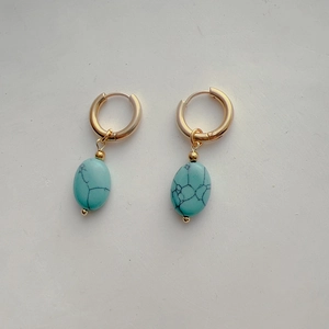 Detailed shot of golden oval earrings featuring textured turquoise stone pendants