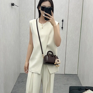 Women's white sleeveless suit set with a brown mini Boston barrel bag and gold hardware