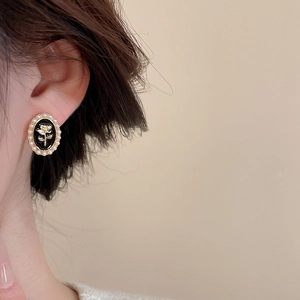 Detail of vintage oval stud earring with golden rose relief, black resin, and white pearls