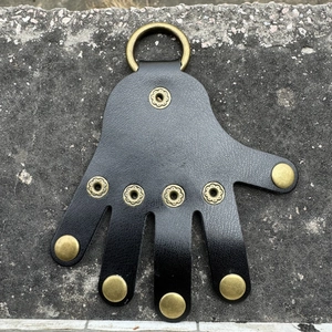 Detail of a black leather palm-shaped key holder with bronze metal ring on stone