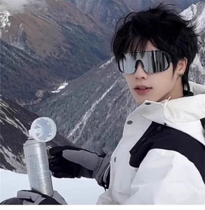 Detail view of silver ski goggles worn with white hooded gear against a snowy mountain backdrop