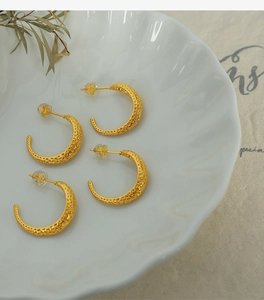 Close-up of gold C-shaped earrings with hammered texture on a white petal plate