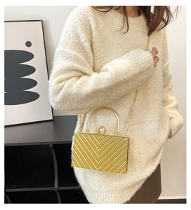 Detailed view of golden chevron acrylic clutch bag with pearl clasp and metal chain strap