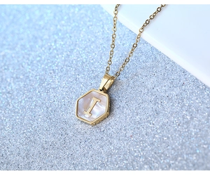 Macro shot of gold hexagon necklace with mother of pearl letter I on shimmering sand