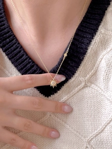 Golden sunburst pendant necklace with zircon on a model wearing a beige sweater