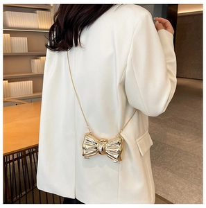 Close-up of golden metallic bow-shaped mini evening bag with fine chain shoulder strap