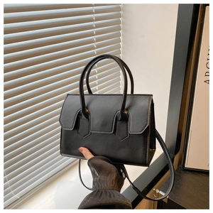 Black leather handbag with top handles and shoulder strap held against a window