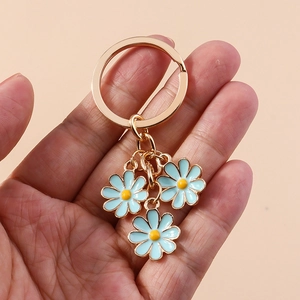Detail of three light blue daisy pendants with golden rings held in hand on orange backdrop