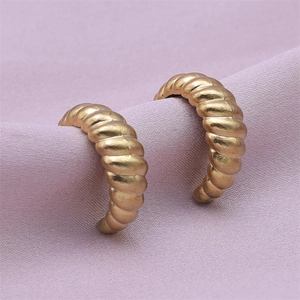 Macro shot of gold textured spiral hoop earrings on purple silk fabric backdrop