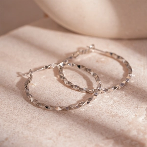 Detail of silver hoop earrings featuring a diamond-cut textured surface on a stone background