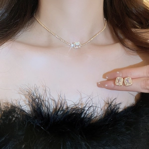 Detail shot of elegant gold necklace and square zircon earrings worn on a female model
