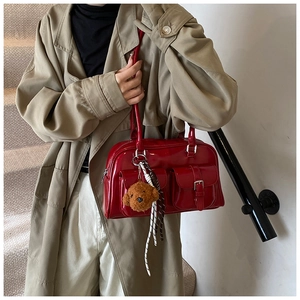 Detail of red glossy pillow bag with front buckle pockets and a cute brown plush bear charm