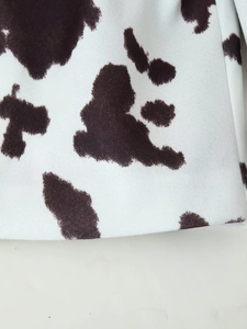 Close-up of the cow print fabric texture in white and dark brown for women's casual jacket