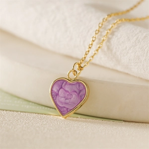 Macro detail of golden chain necklace featuring a purple enamel heart swirl pendant