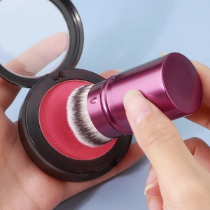 Close-up of soft retractable makeup brush picking up powder from a round blush case