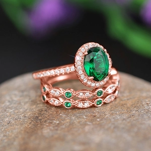 Macro shot of rose gold rings set featuring an oval green emerald and delicate diamonds